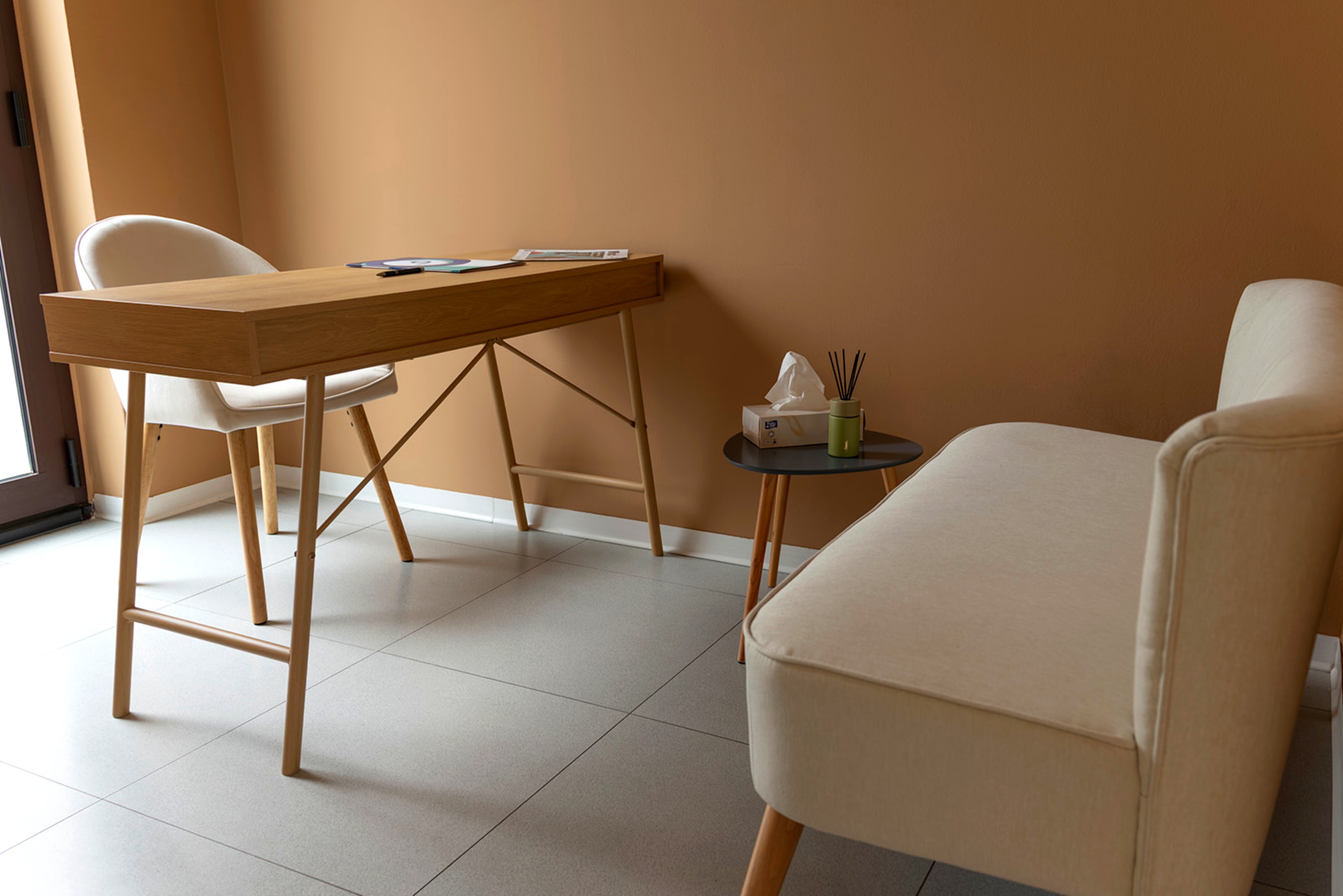 Interno dello studio: scrivania in legno chiaro, poltroncina e divanetto su parete color terracotta